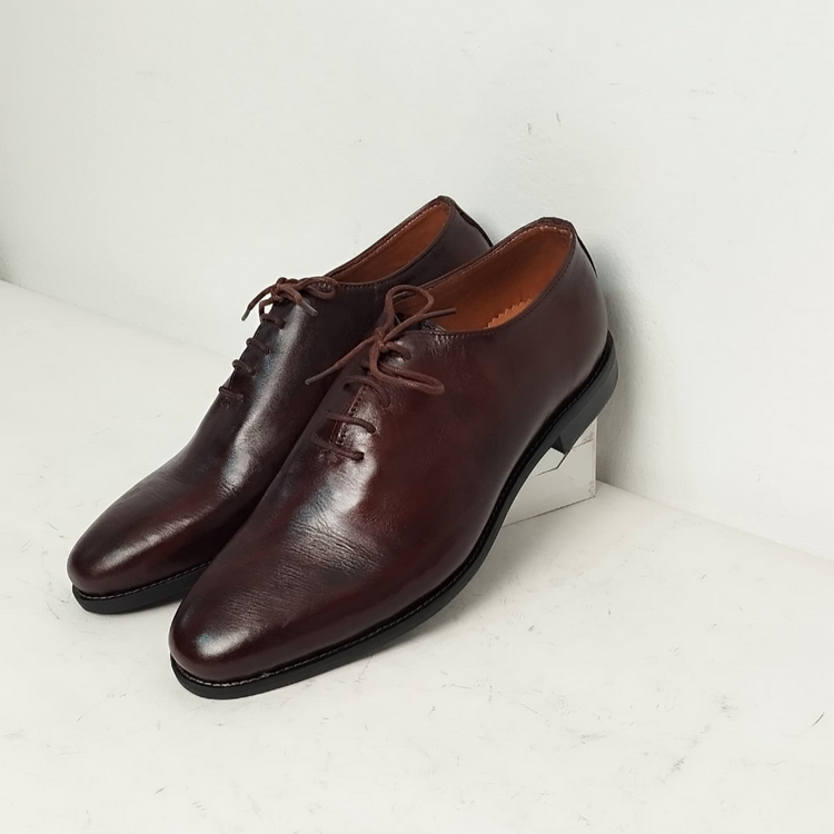 A pair of brown, whole cut oxford shoes with lace-up closure, placed against a white background.